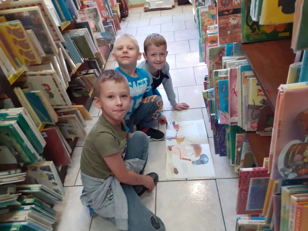 Dzieci z SP Nr 7 czytające książkę, pomiędzy regałami w Filii Nr 4 - powiększenie