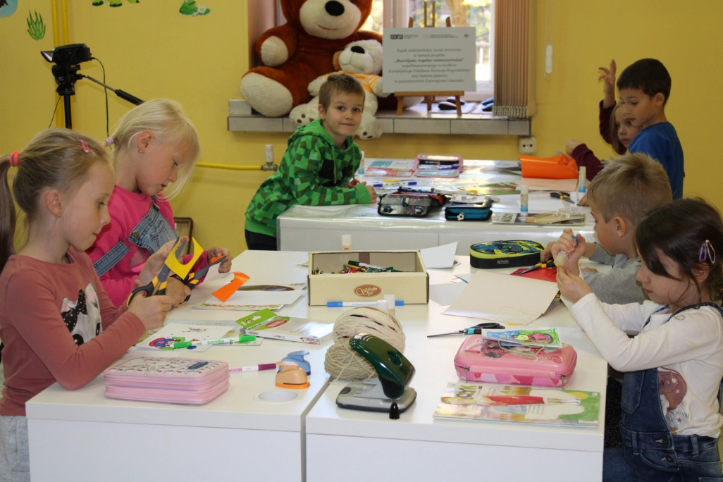 Grupa uczniów wykonująca swoje prace przy stołach w Oddziale dla Dzieci - powiększenie