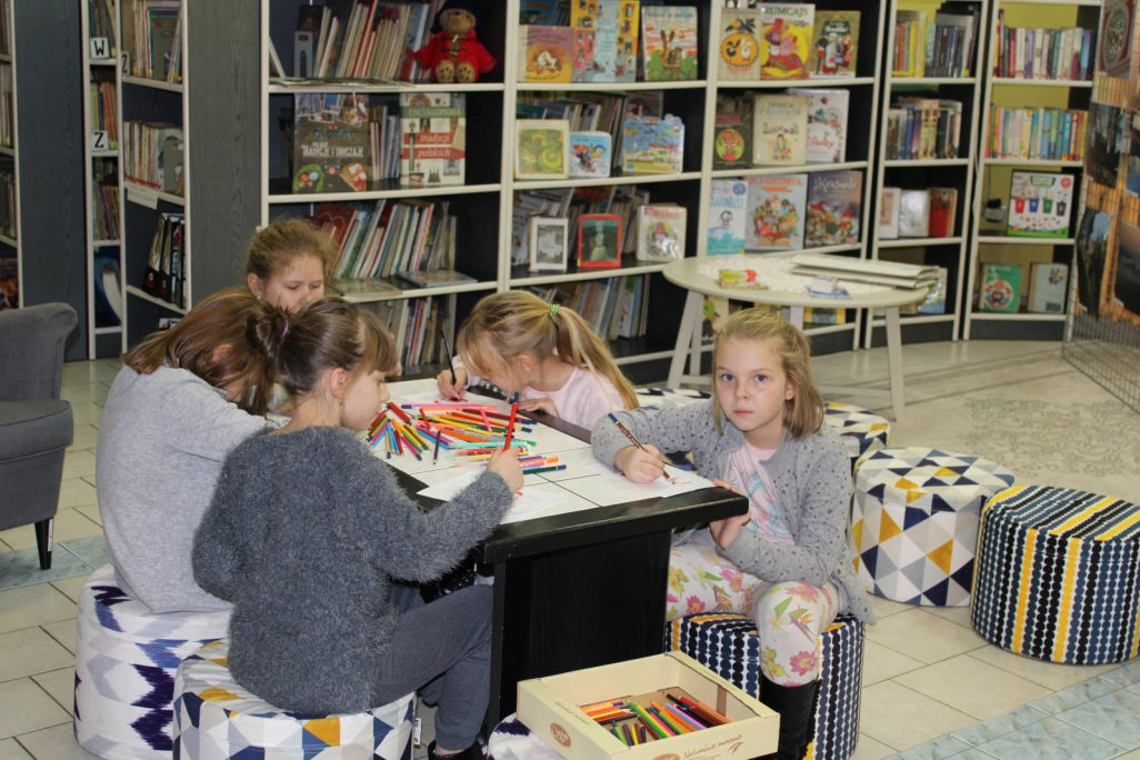 Grupa uczestników zajęć wykonuje kolorowanki przy stole w Oddziale dla Dzieci - powiększenie