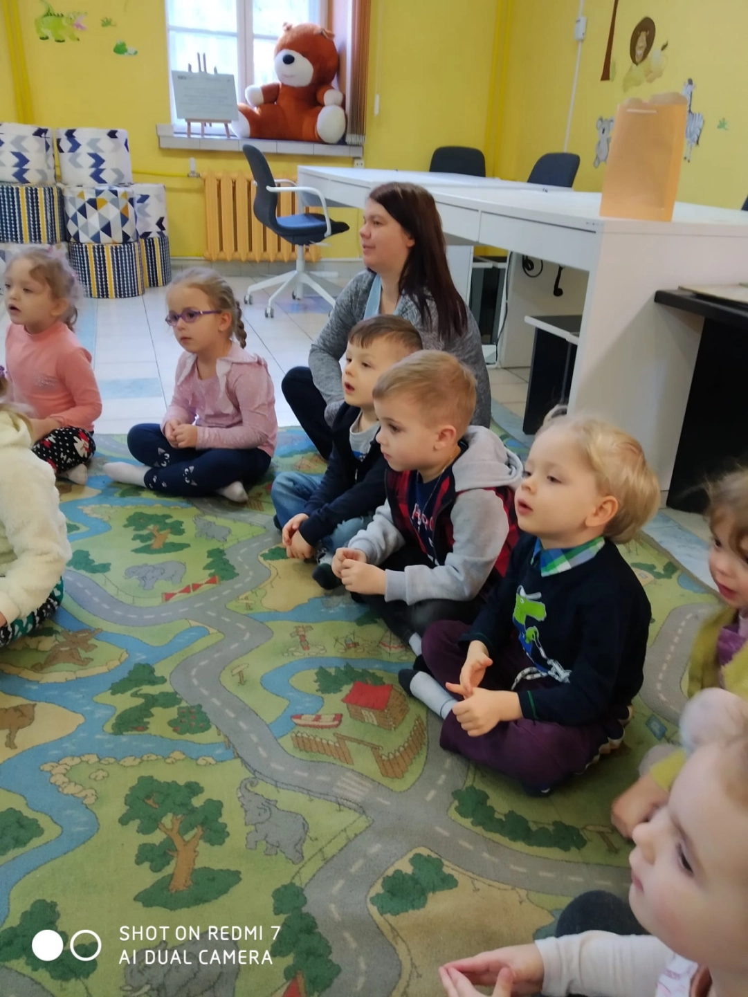 Przedszkolaki siedzą na dywanie w Oddziale dla Dzieci - powiększenie