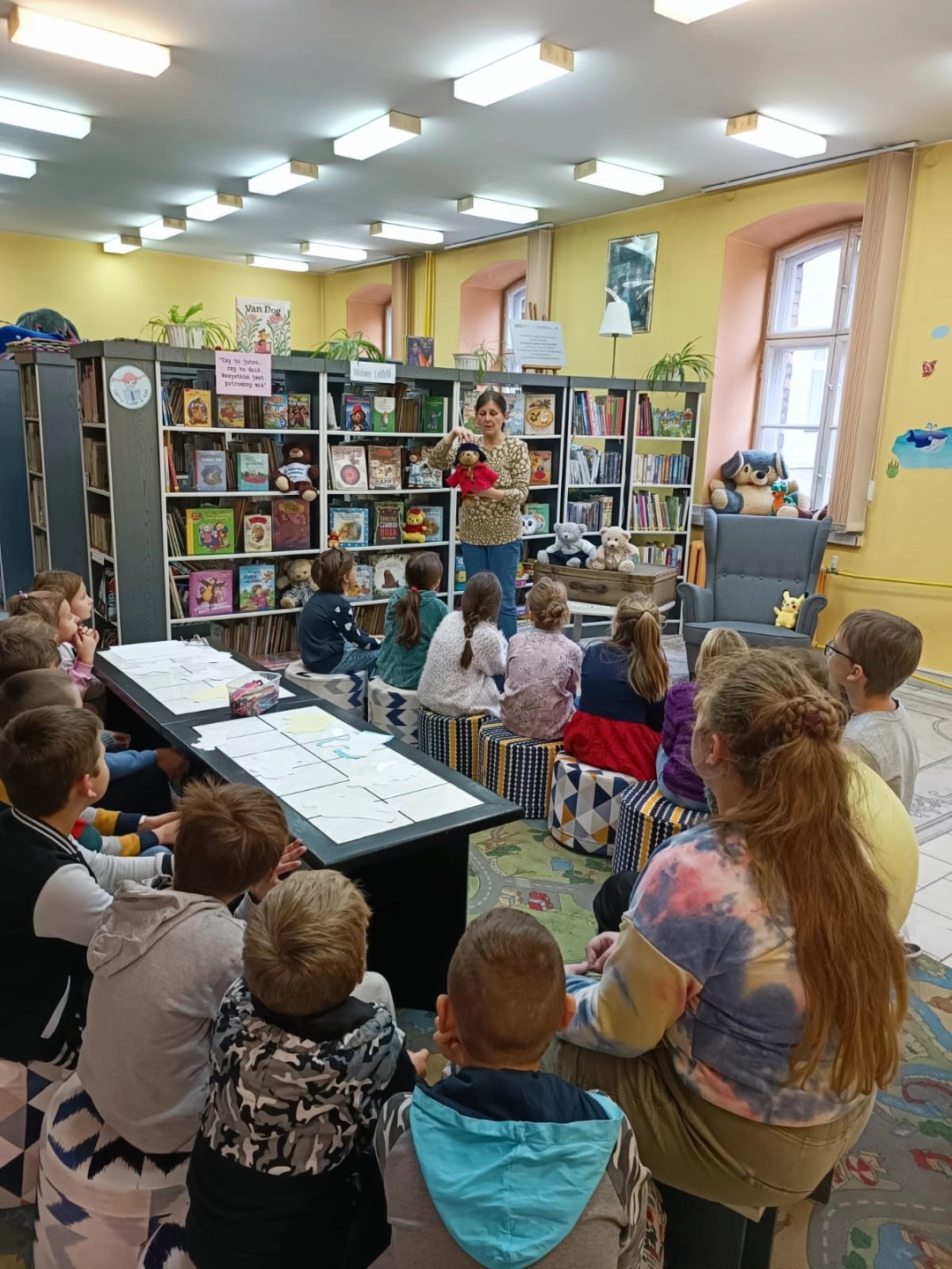 Dzieci siedzące na pufach patrzą na prowadzącą lekcję biblioteczną - powiększenie