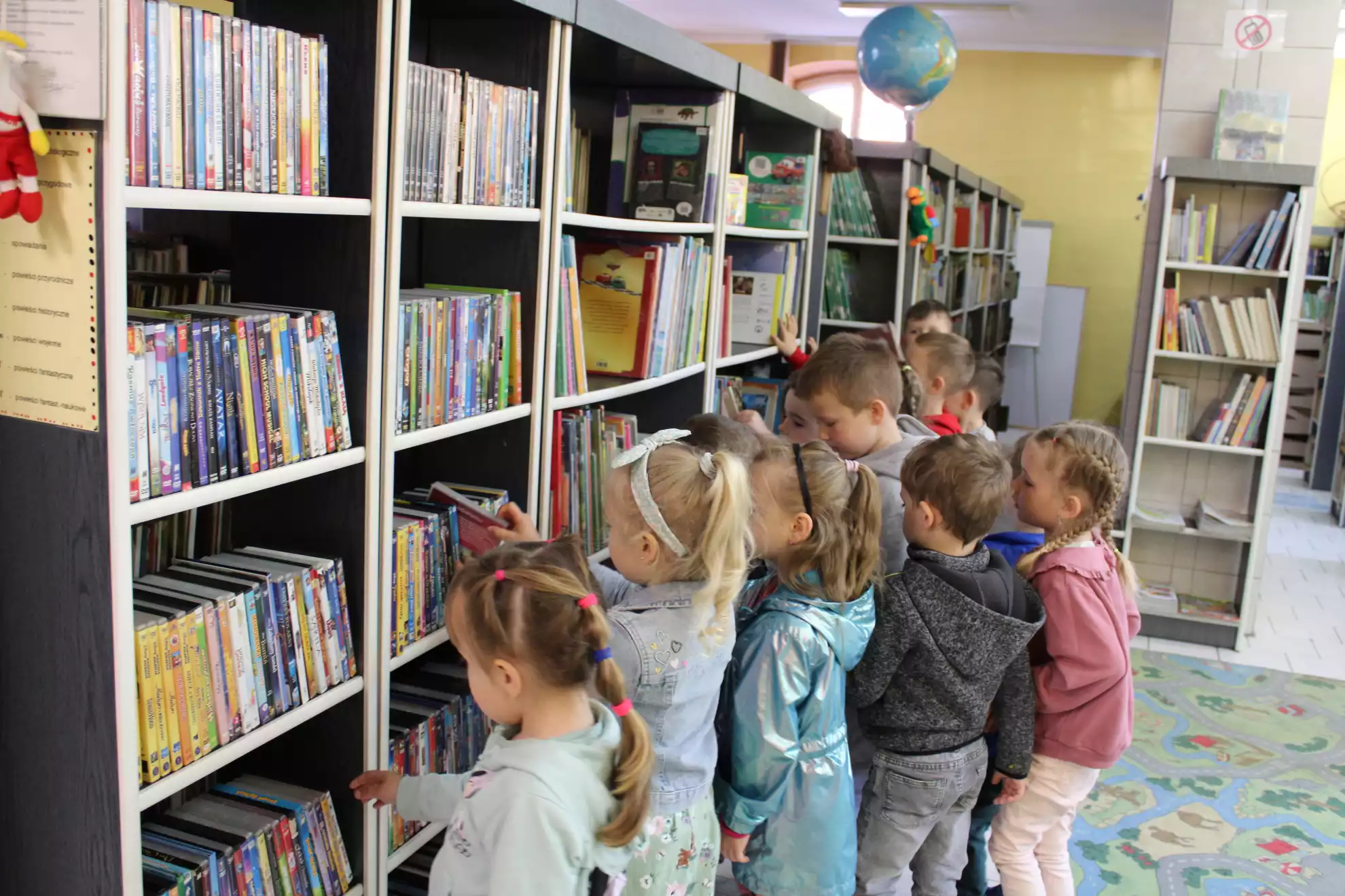 Dzieci stoją przy regale z książkami i wybierają bajeczki - powiększenie