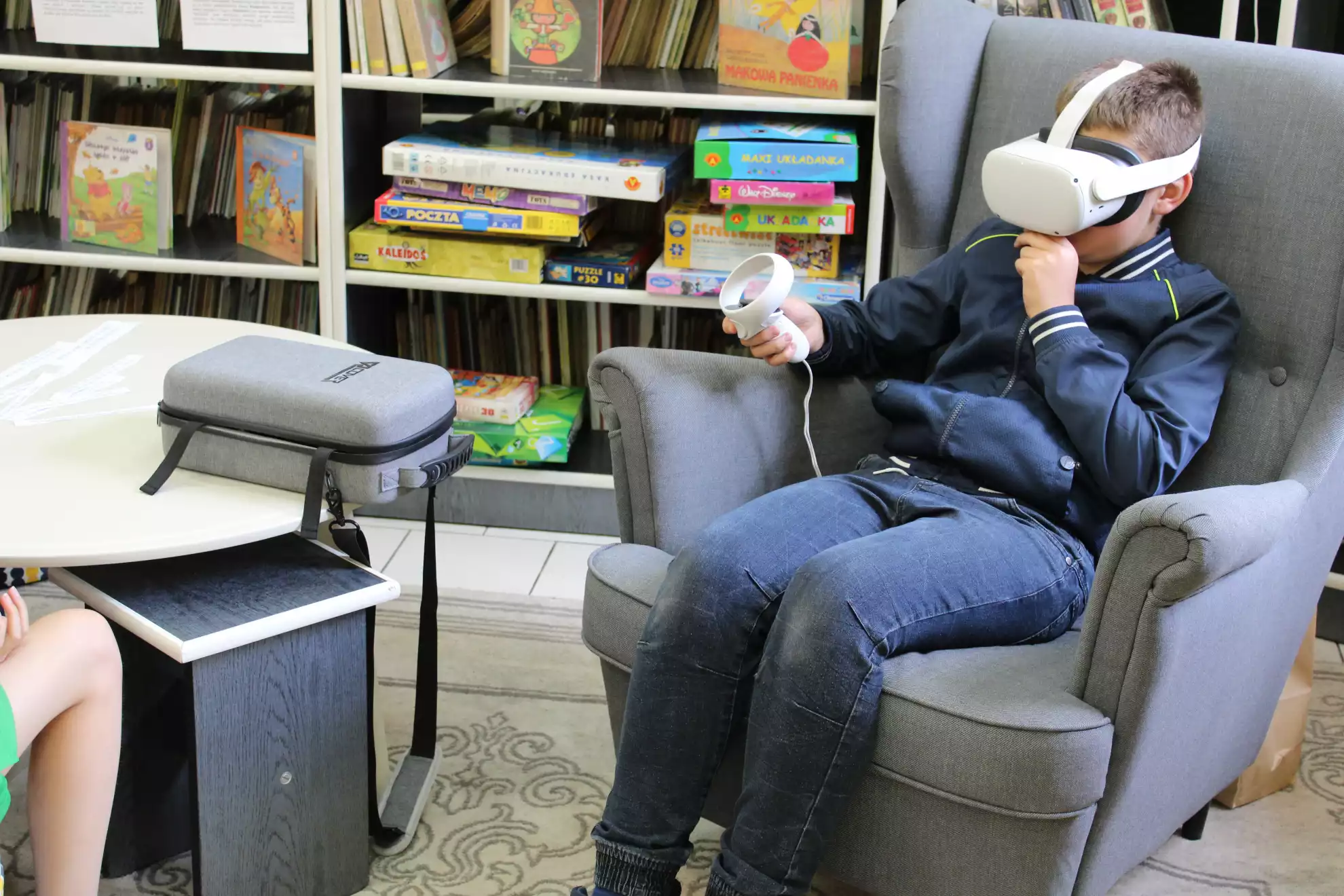 Uczeń siedzi w fotelu. Na głowie ma okulary VR, a w ręce kontroler. - powiększenie