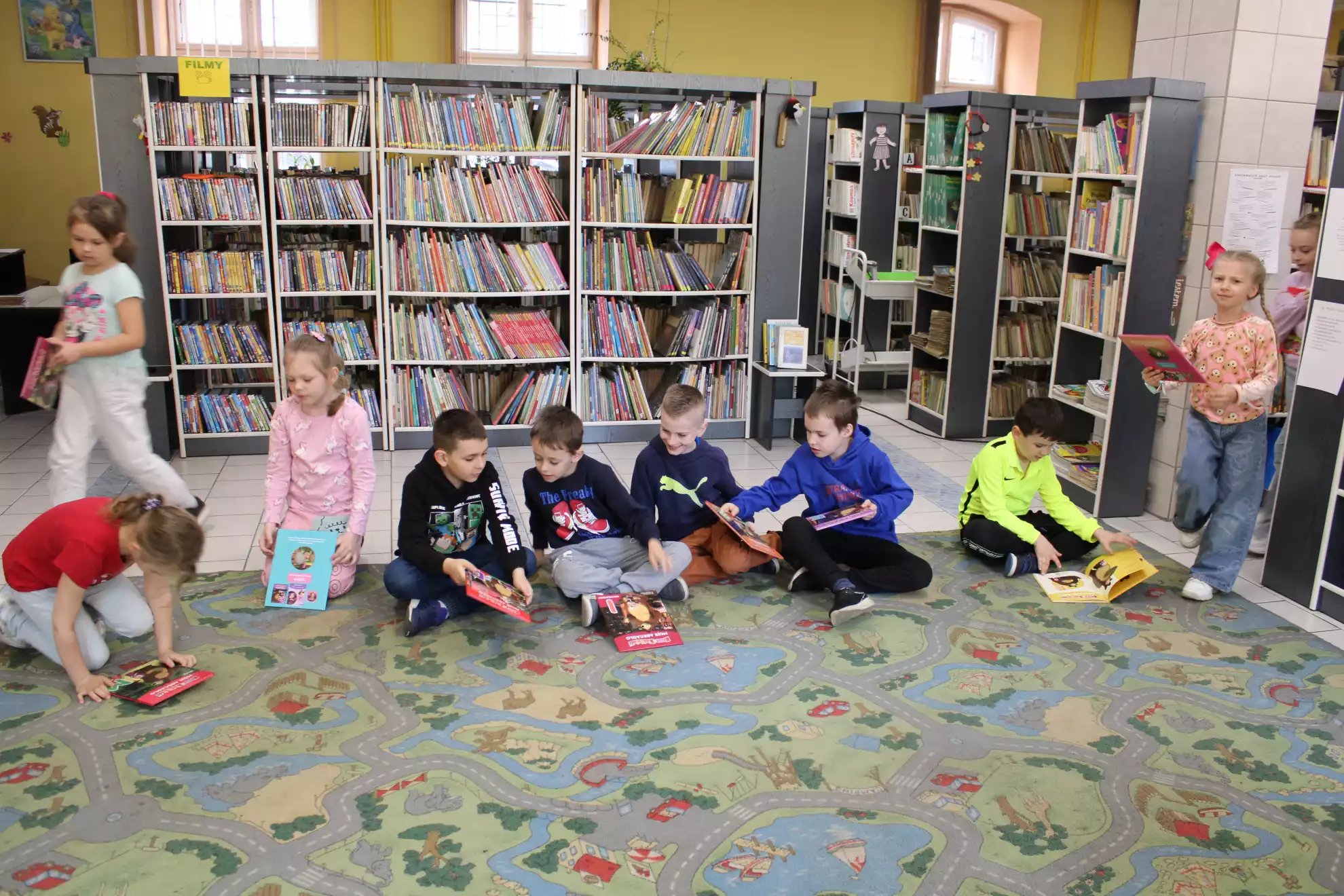 Dzieci siedzą na dywanie i przeglądają książki. - powiększenie