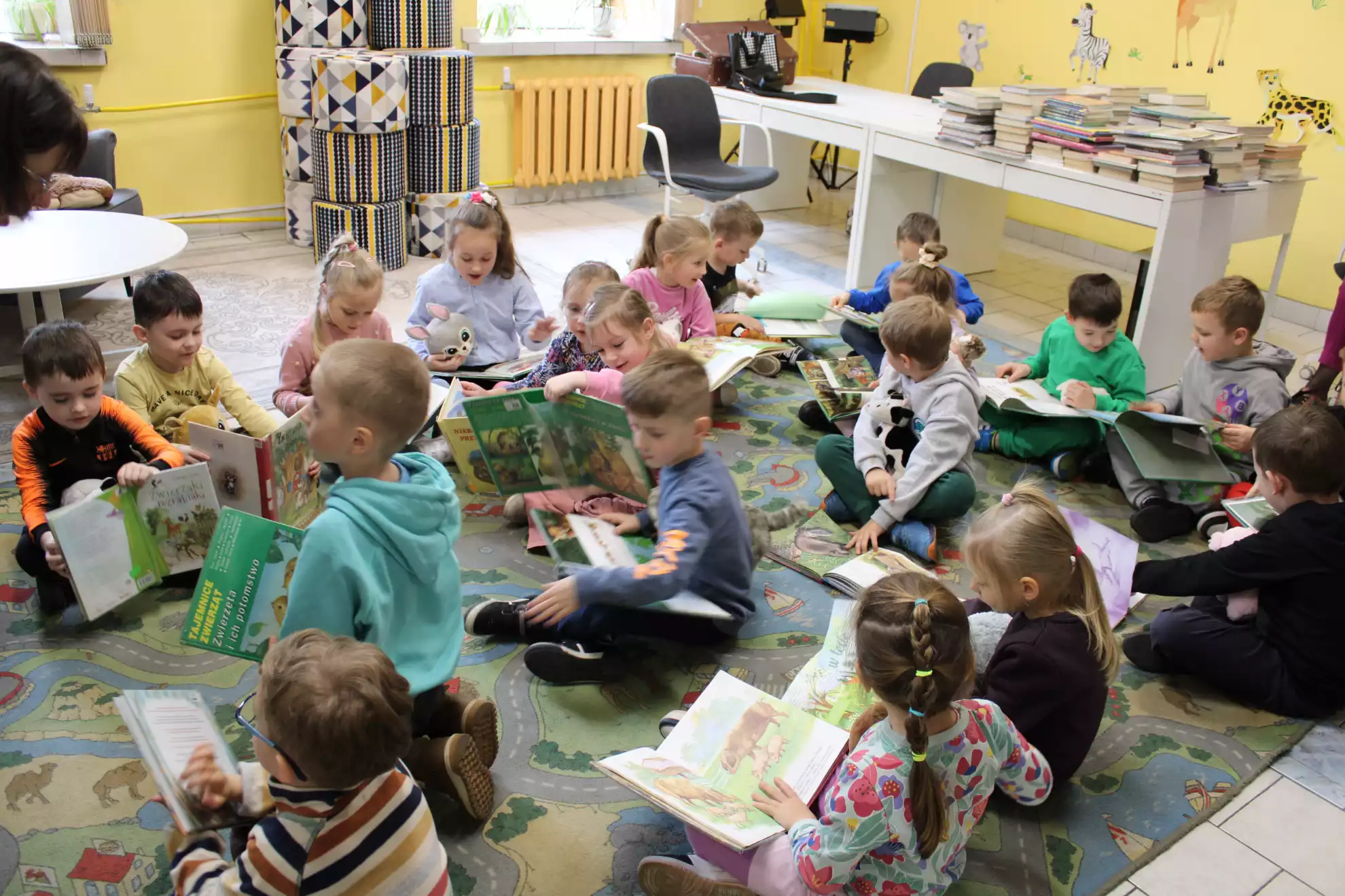 Dzieci siedzą na dywanie i oglądają książki.  - powiększenie