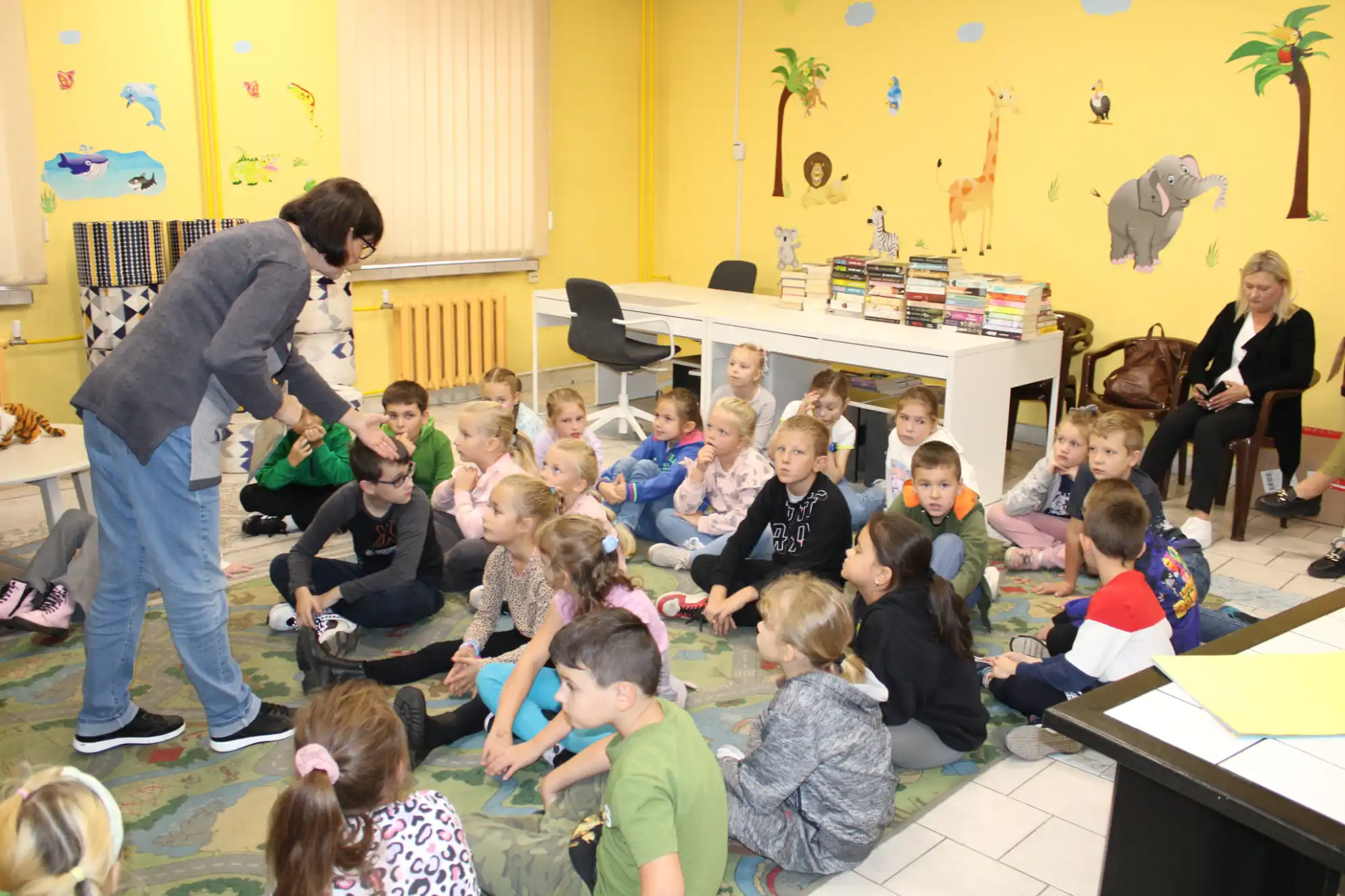 Dzieci siedzą na dywanie i rozmawiają z panią bibliotekarką. - powiększenie