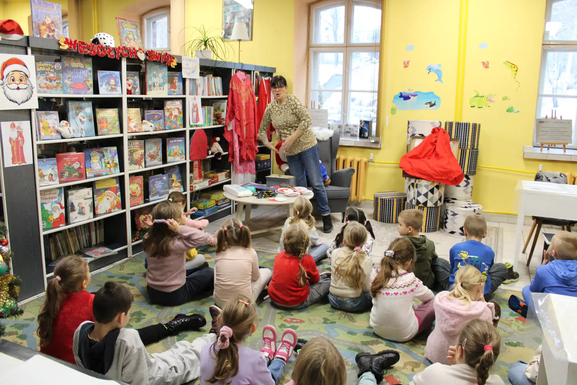 Dzieci siedzą na dywanie i oglądają stroje Świętego Mikołaja.  - powiększenie