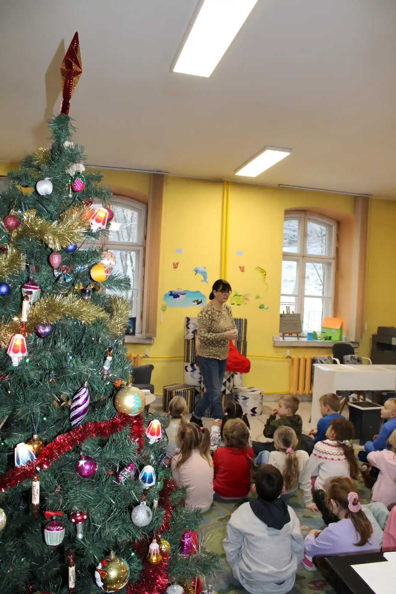 Dzieci siedzą na dywanie i oglądają stroje Świętego Mikołaja.  - powiększenie