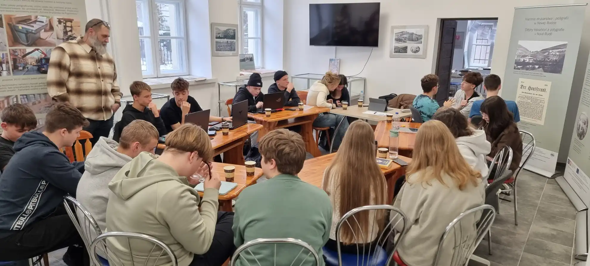 Maciej Zarański prowadzi zajęcia z uczniami, siedzącymi przy stołach. - powiększenie