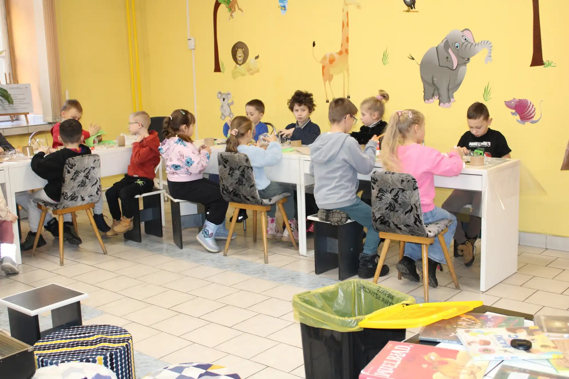 Grupa dzieci siedzi przy stołach podczas warsztatów w bibliotece. - powiększenie