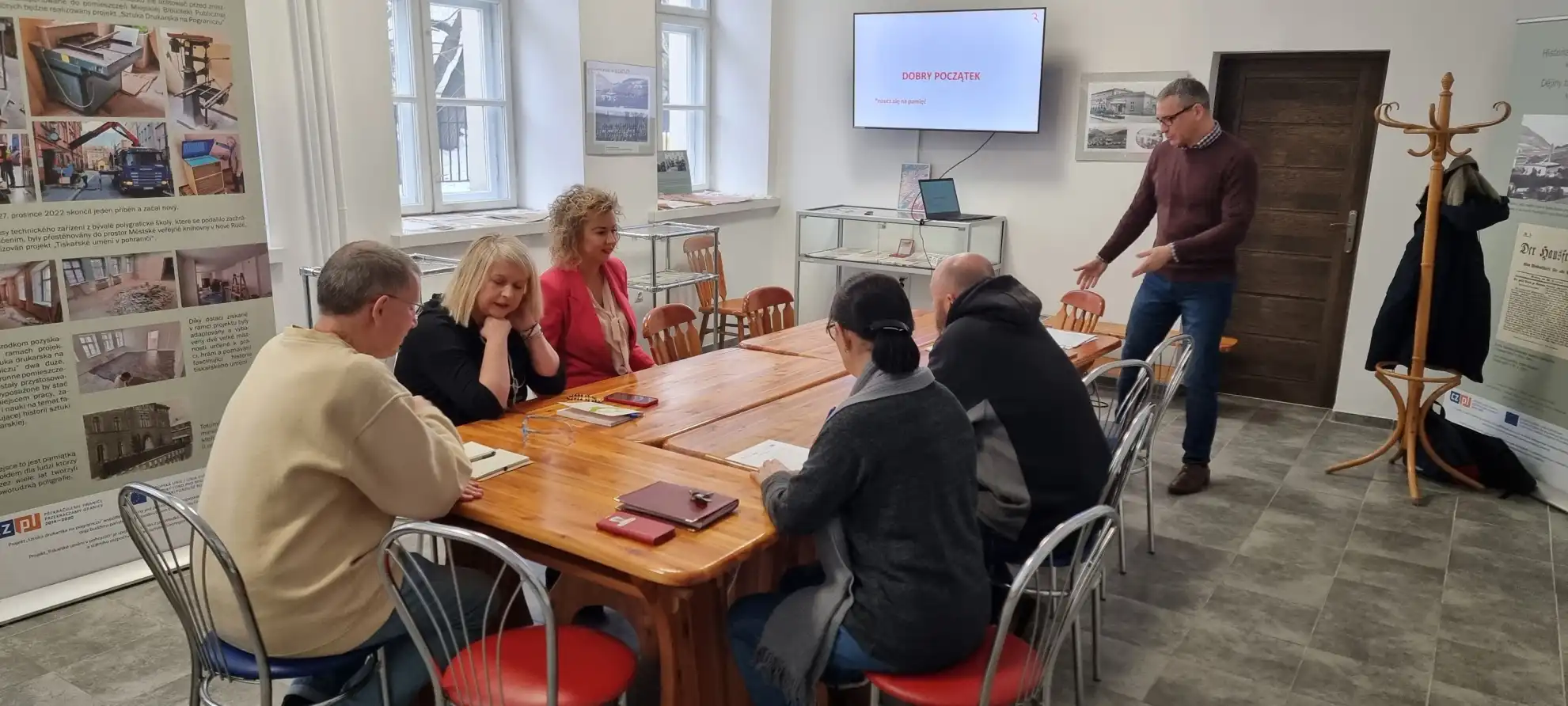 Pracownicy biblioteki siedzą przy stole podczas trwania szkolenia. przy nich stoi prowadzący. - powiększenie