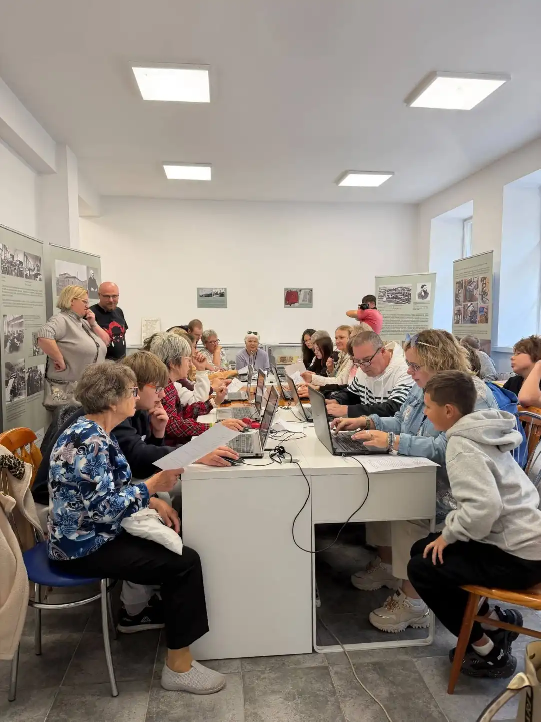Grupa seniorów wraz z młodzieżą wspólnie pracują przy laptopach - powiększenie