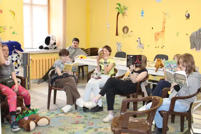 Młodzież siedzi na krzesłach i przegląda książki.