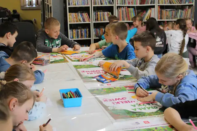 Dzieci siedzą przy stolikach i wykonują prace plastyczne kredkami. 
