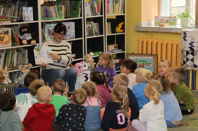 Pani bibliotekarka pokazuje dzieciom ilustracje w książce. 