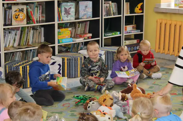 Dzieci siedzą na dywanie i oglądają książeczki. 