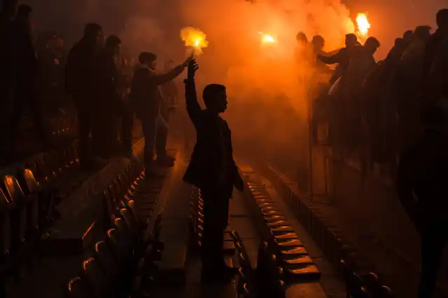 Fotografia przedstawiająca kibiców na stadionie z odpalonymi racami.