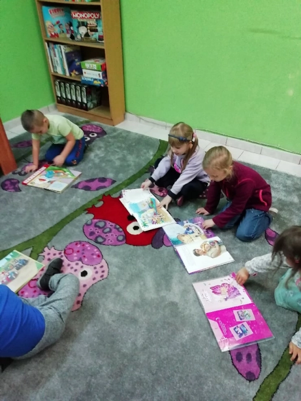 Przedzkolaki przeglądający bajeczki dla najmłodszych, siedzący na dywanie w Filii Nr 4