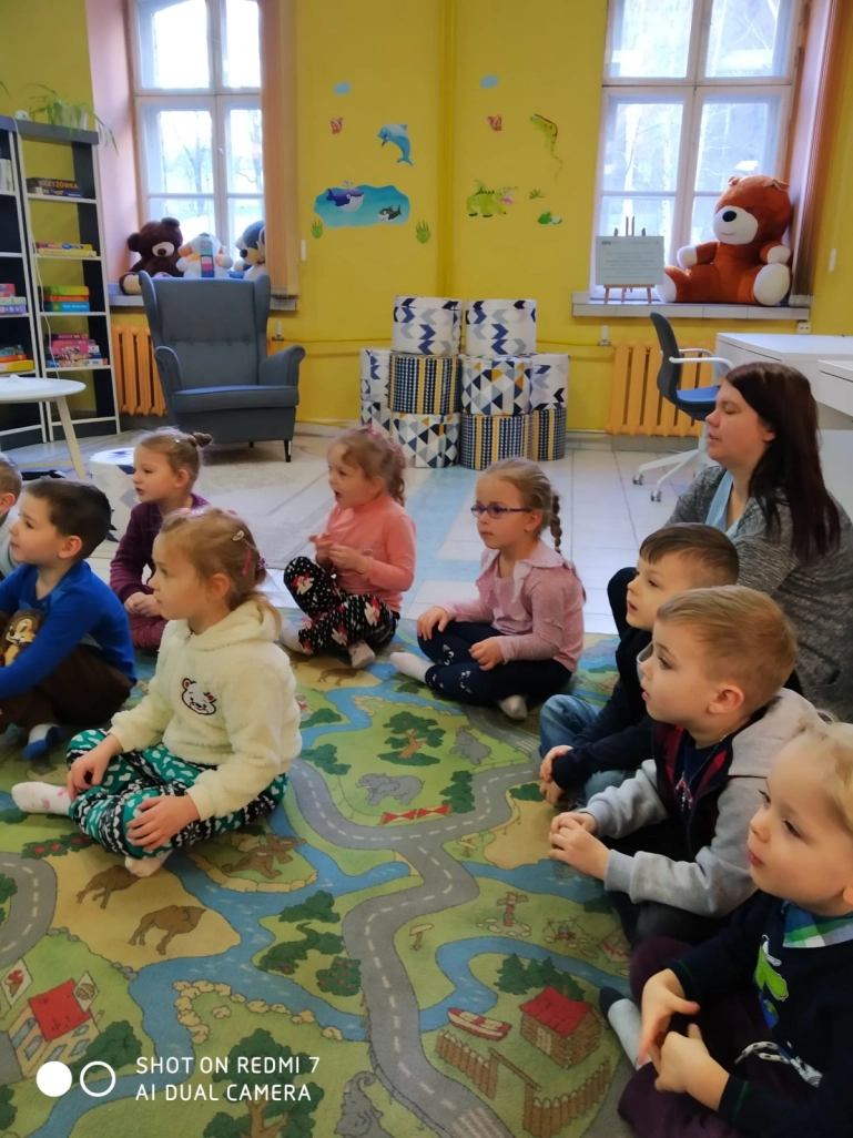 Przedszkolaki siedzą na dywanie w Oddziale dla Dzieci