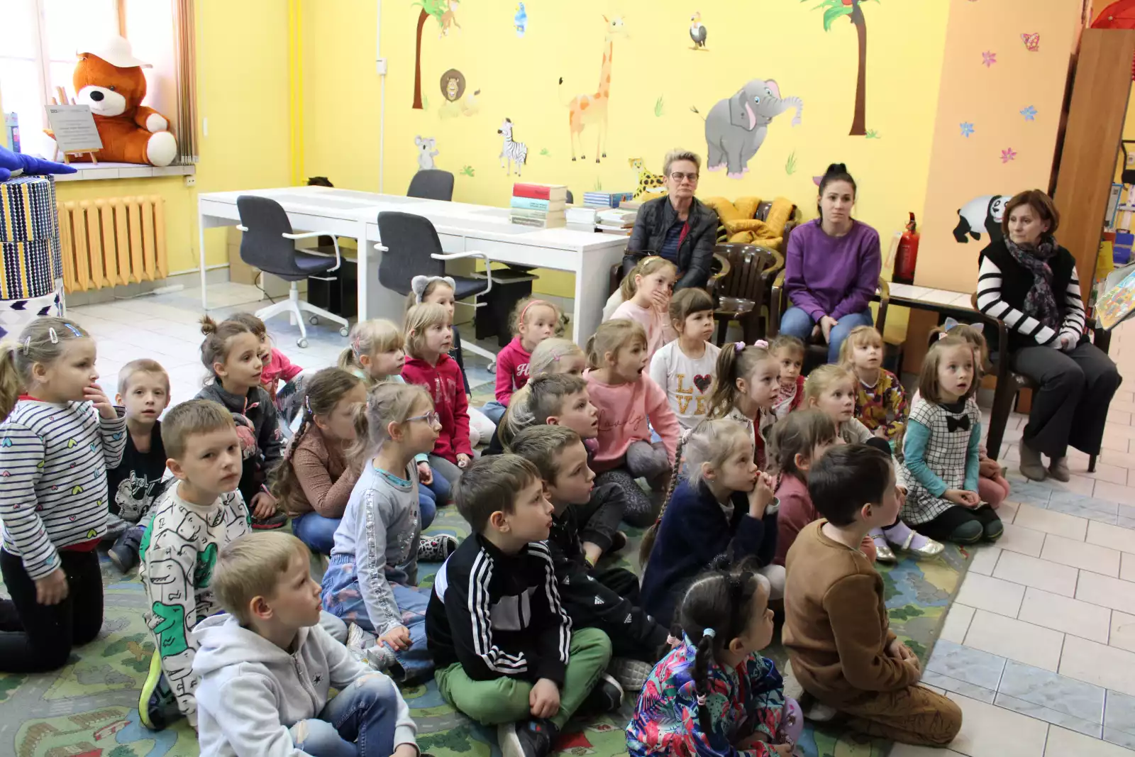 Grupa dzieci słucha prowadzącej zajęcia