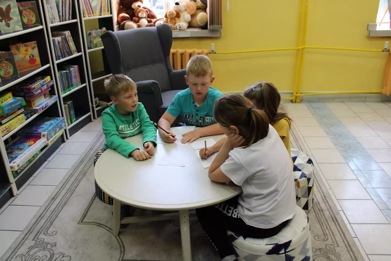 Dzieci siedzą przy stoliku i rozwiązują krzyżówkę