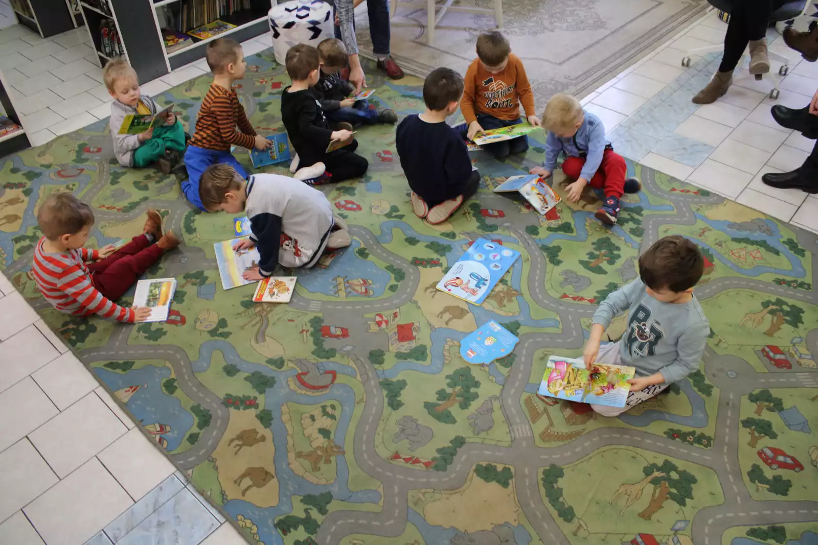 Dzieci siedzą na dywanie i oglądają książeczki. 