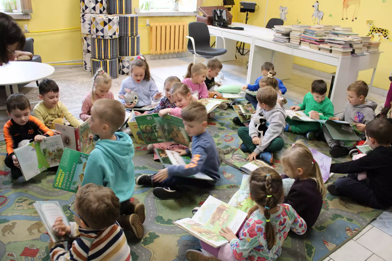 Dzieci siedzą na dywanie i oglądają książki. 