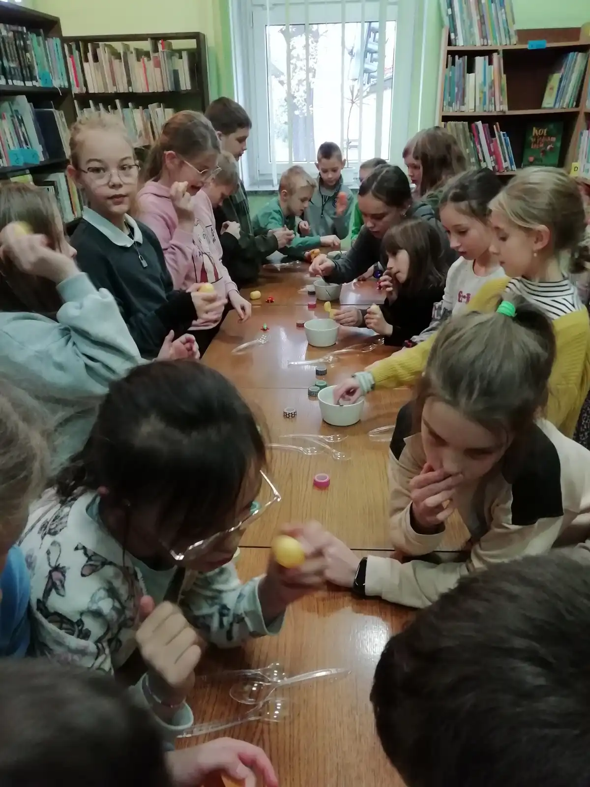 Dzieci siedzą przy stolikach i wykonują prace plastyczne. 