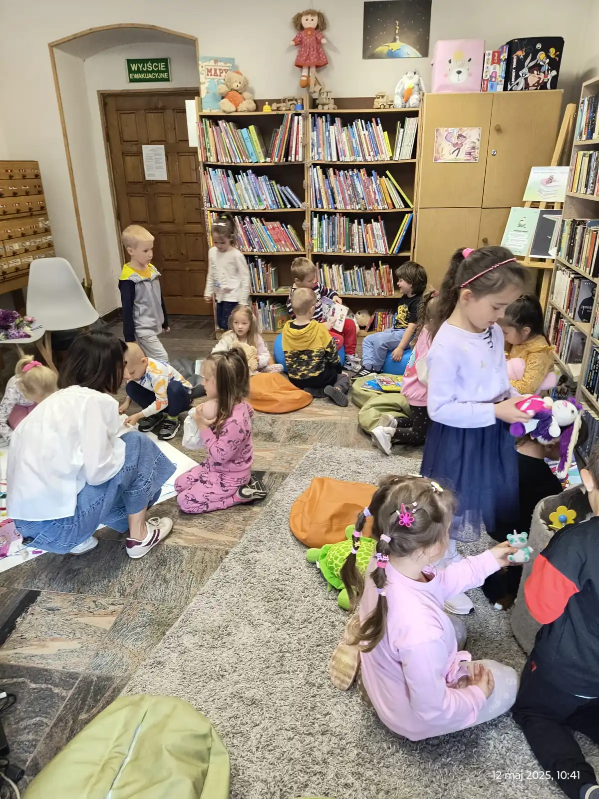 Dzieci siedzą na pufkach i oglądają książeczki. 