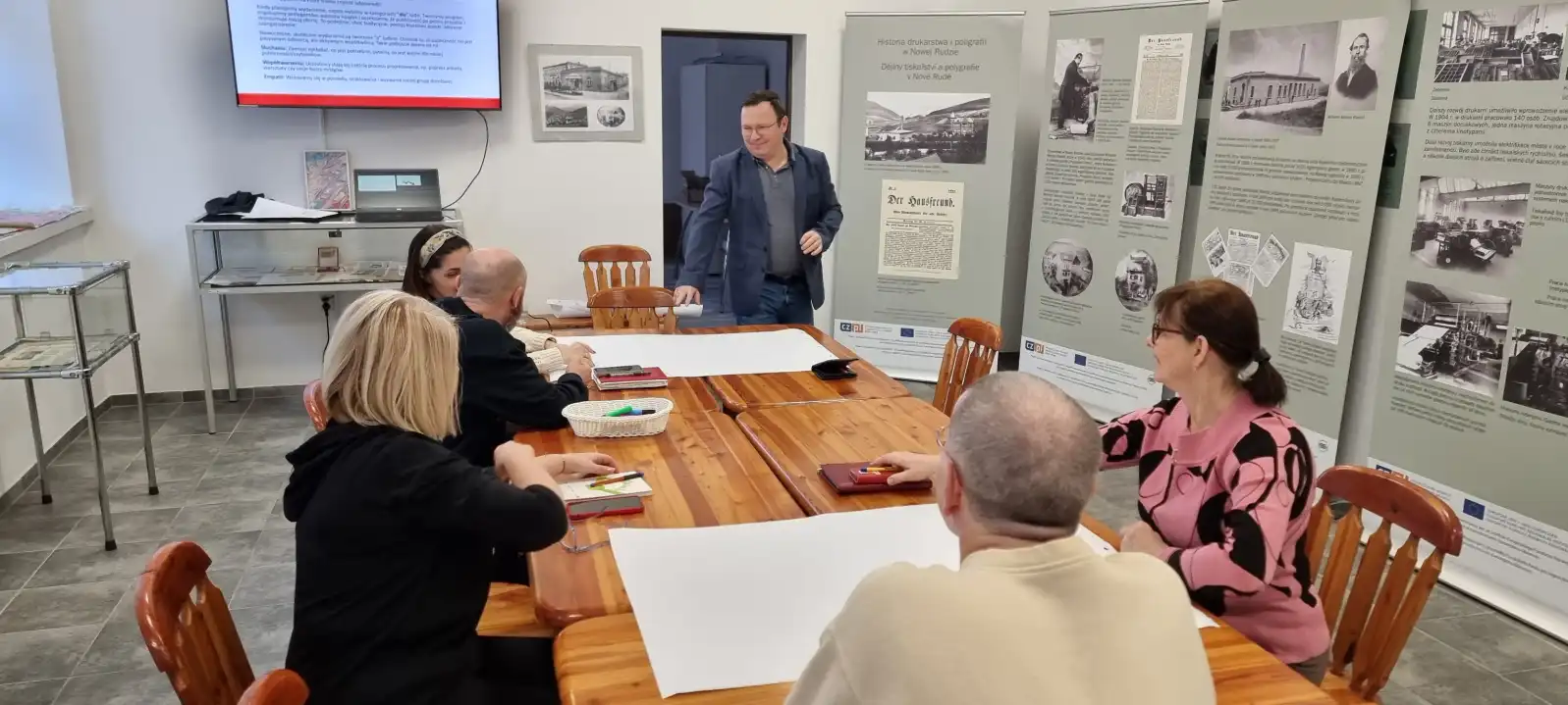 Grupa bibliotekarzy siedzi przy stole w trakcie szkolenia.