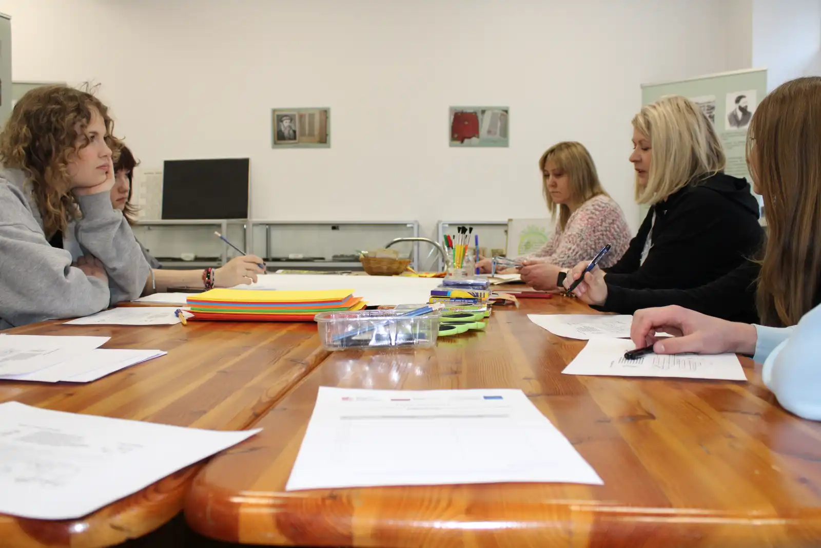 Grupa młodzieży, bibliotekarka i nauczycielka siedzą przy stole w Sali Poligrafii i Drukarstwa.