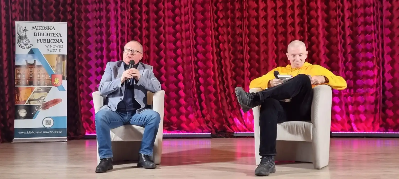 Karol Maliszewski i David Magen siedzą w fotelach na scenie Sali Widowiskowej MBP.