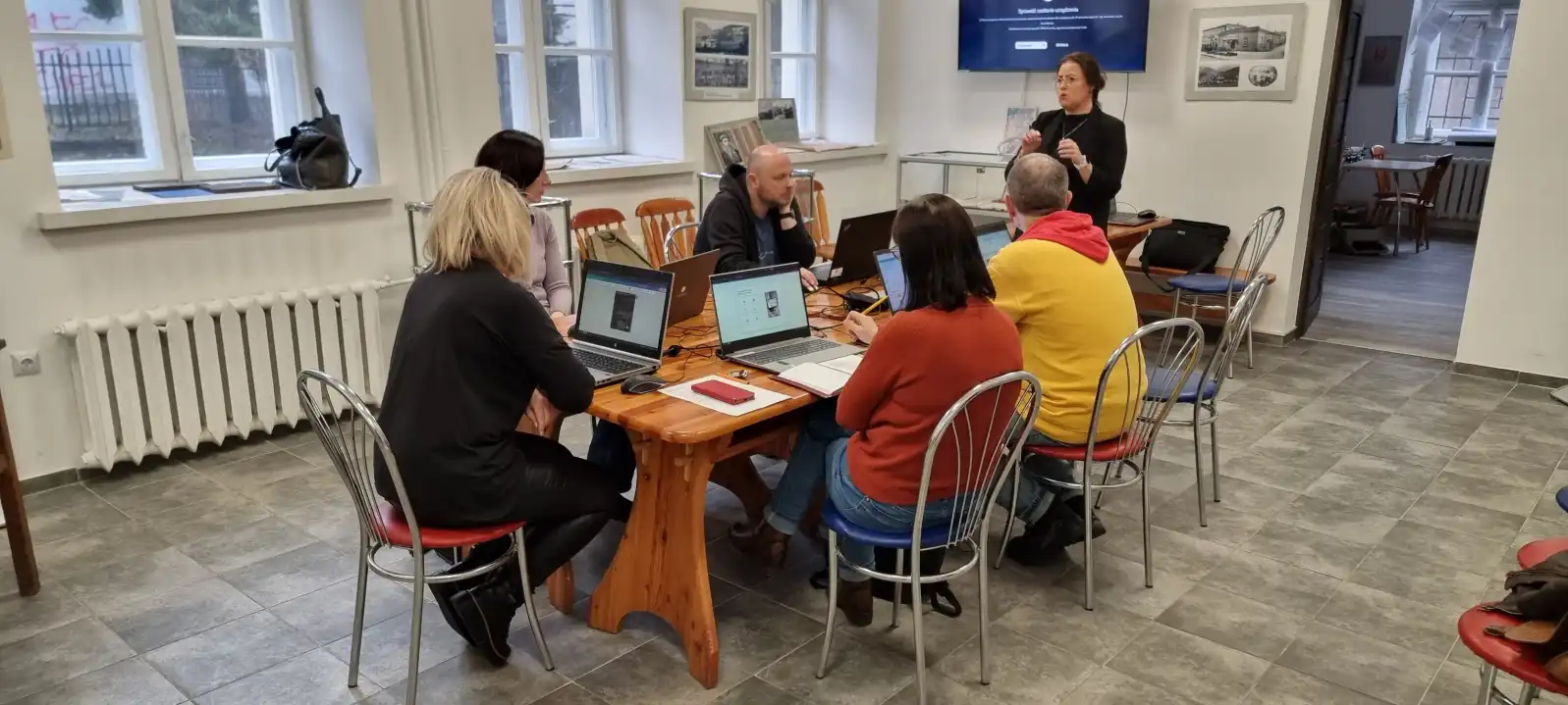 Grupa bibliotekarzy siedzi przy laptopach podczas szkolenia.