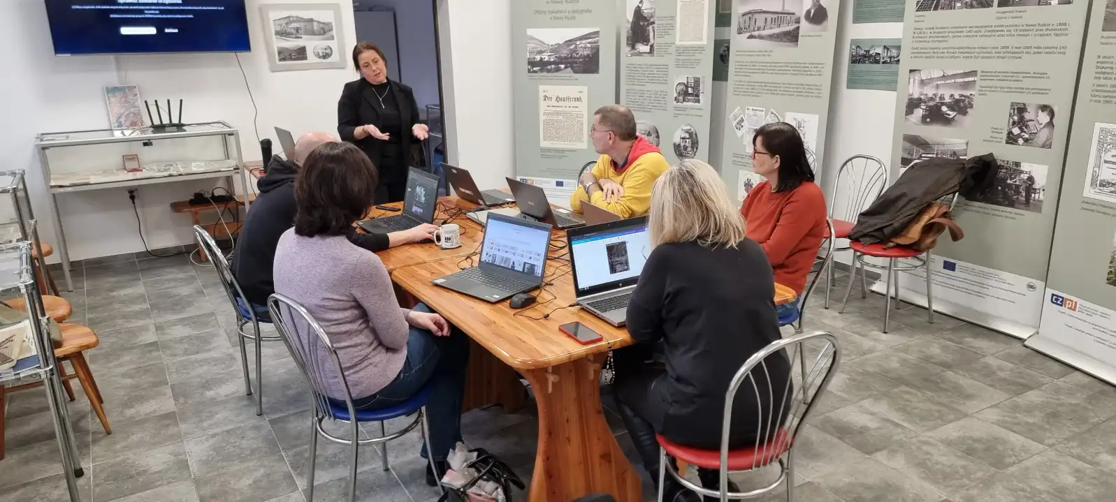 Grupa bibliotekarzy siedzi przy laptopach podczas szkolenia.