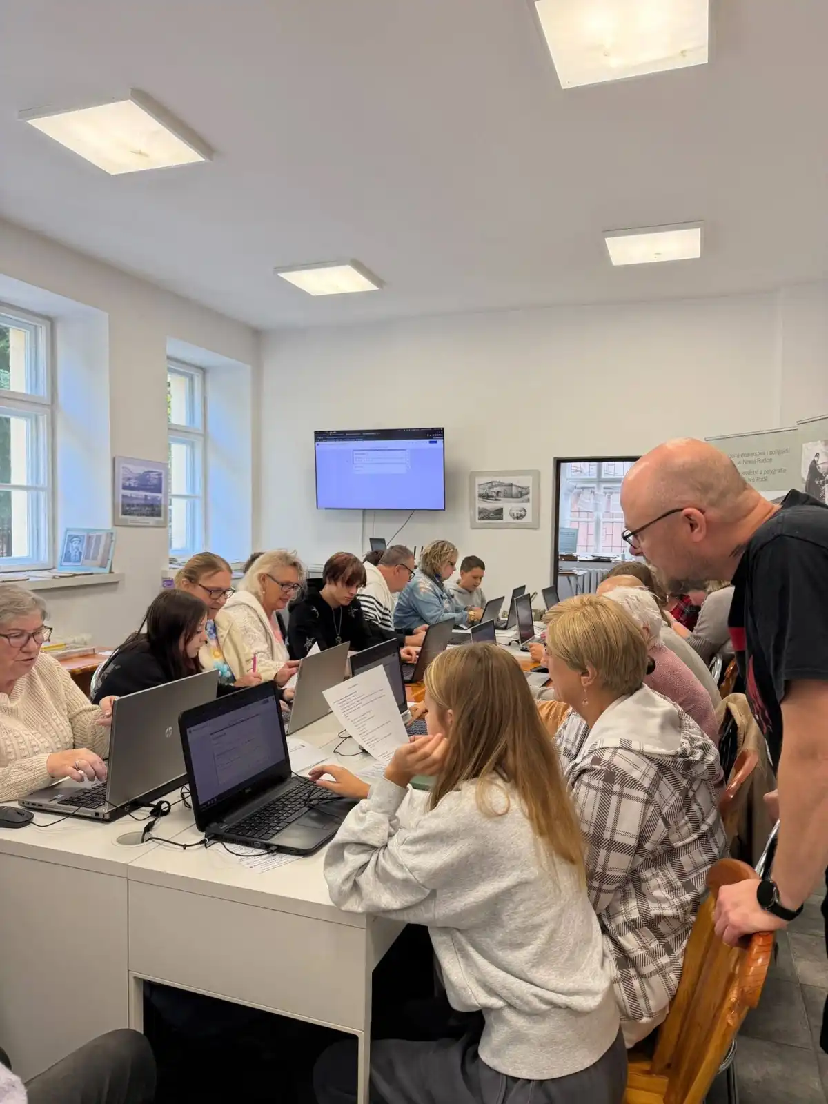 Grupa seniorów wraz z młodzieżą wspólnie pracują przy laptopach