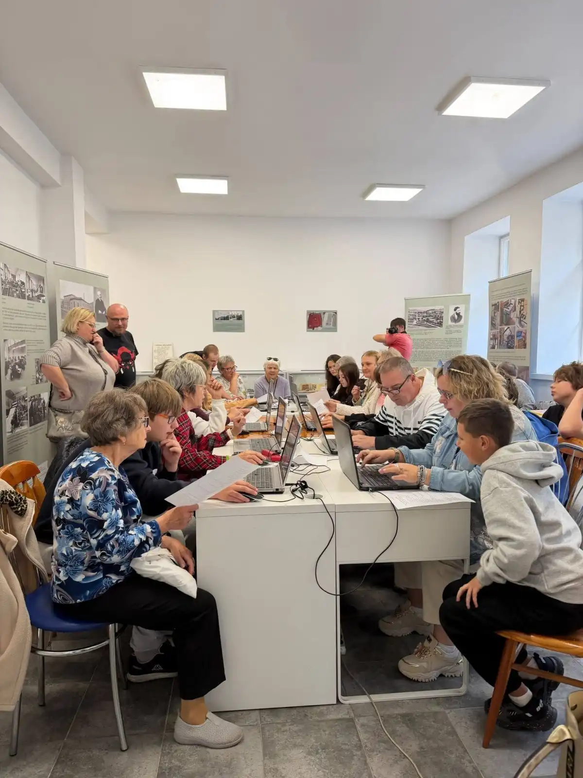 Grupa seniorów wraz z młodzieżą wspólnie pracują przy laptopach